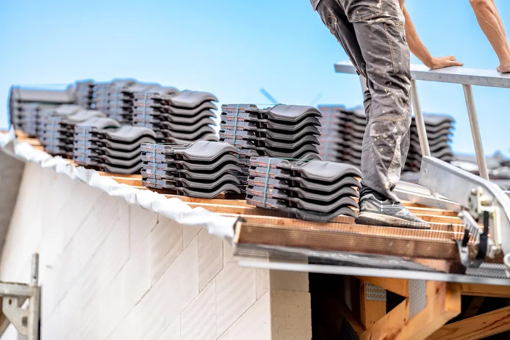 Roofer unloading bundles of roof tiles from a conveyor lift onto a roof